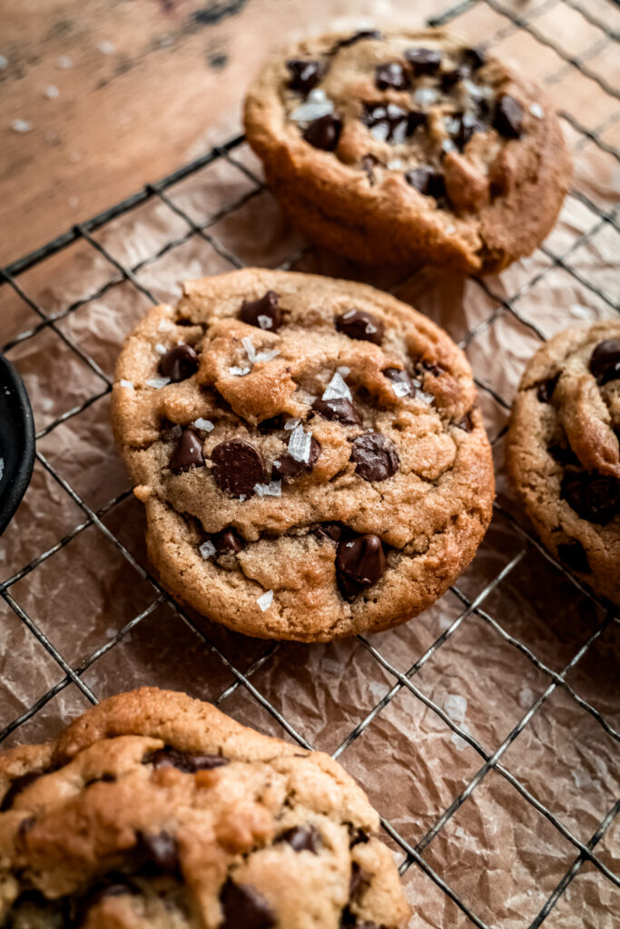 side shot of four chocolate chip cookies on cooling rack with brown parchment paper underneath