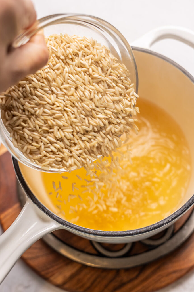 rice being poured into a pot with chicken broth on stove for hot honey chicken bowls