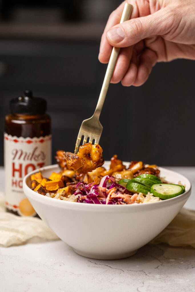 a hand holding a fork getting a bite of chicken from hot honey chicken bowls