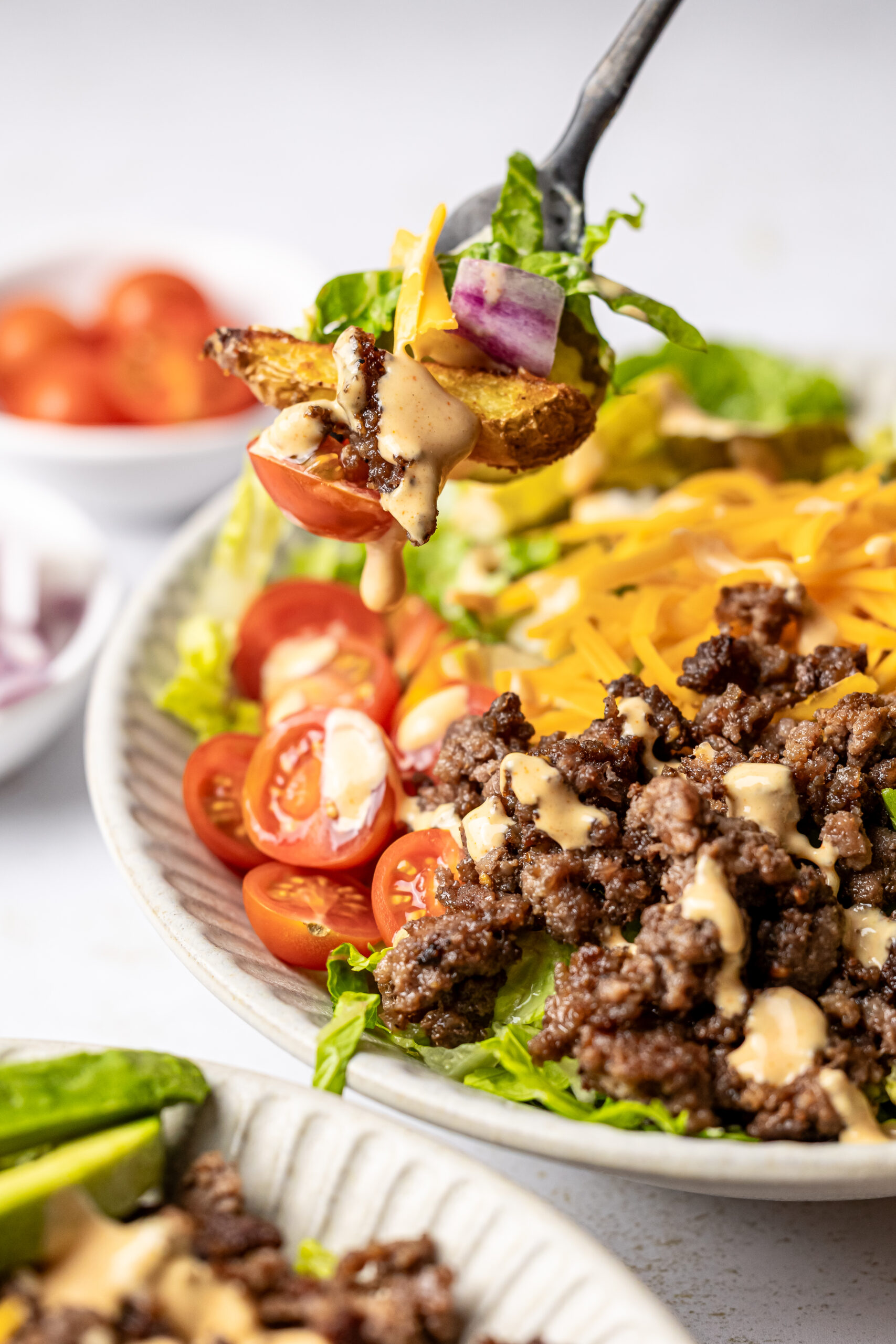 a fork full of burger bowl ingredients in front of burger bowl drizzled with special sauce