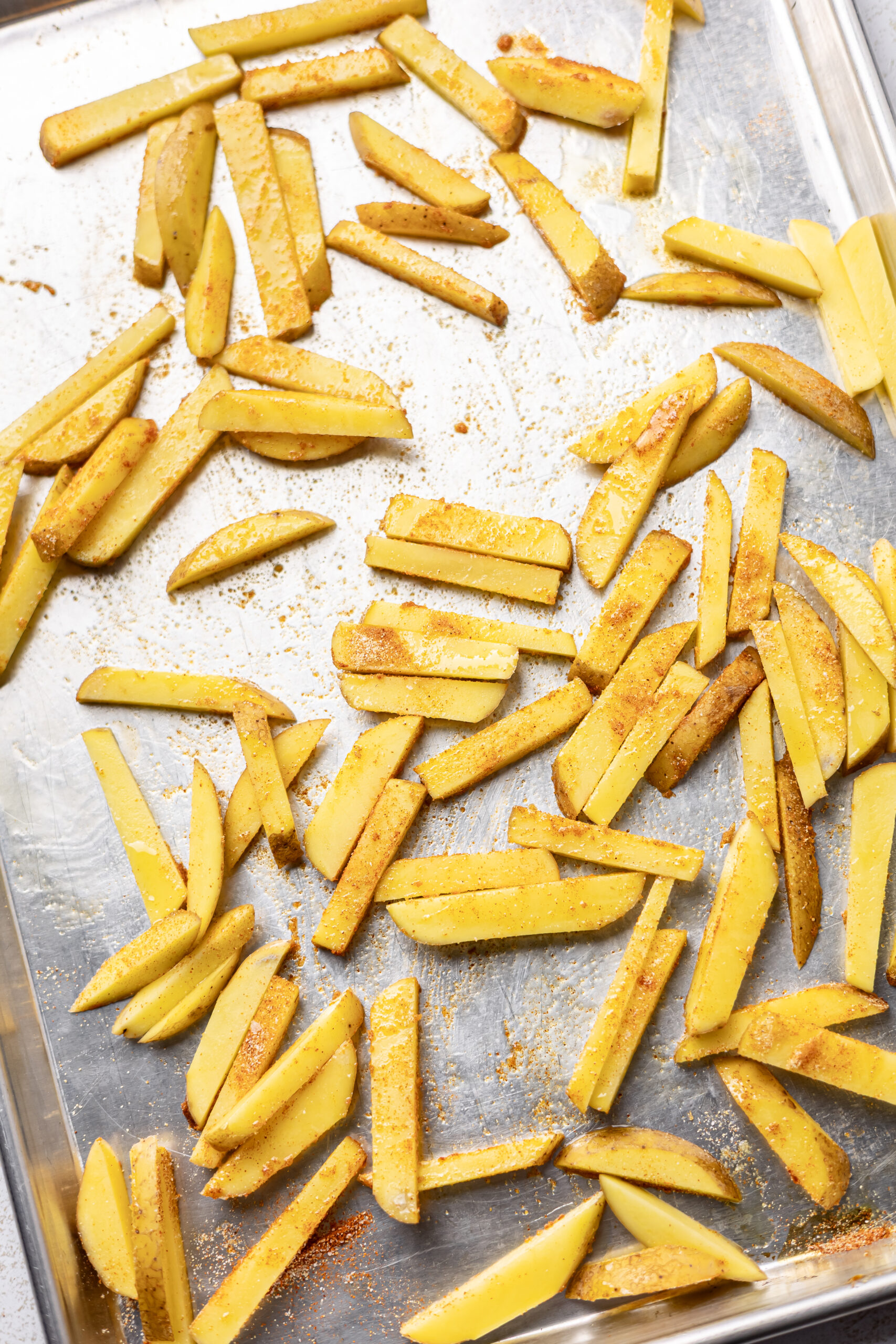 raw french fries seasoned on baking sheet for burger bowl