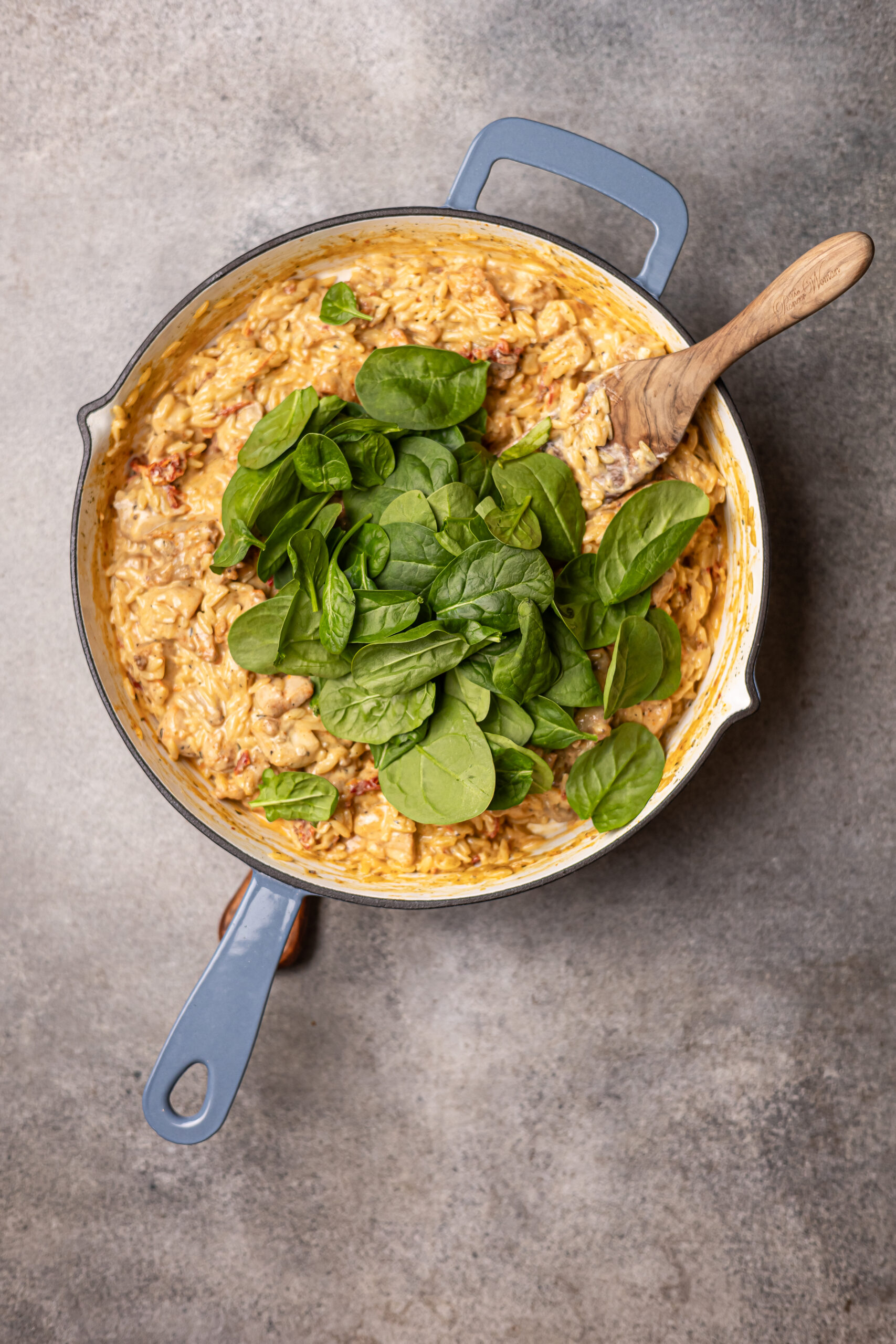 marry me chicken orzo in grey skillet, fresh spinach is on top. There's a wooden spoon in the skillet