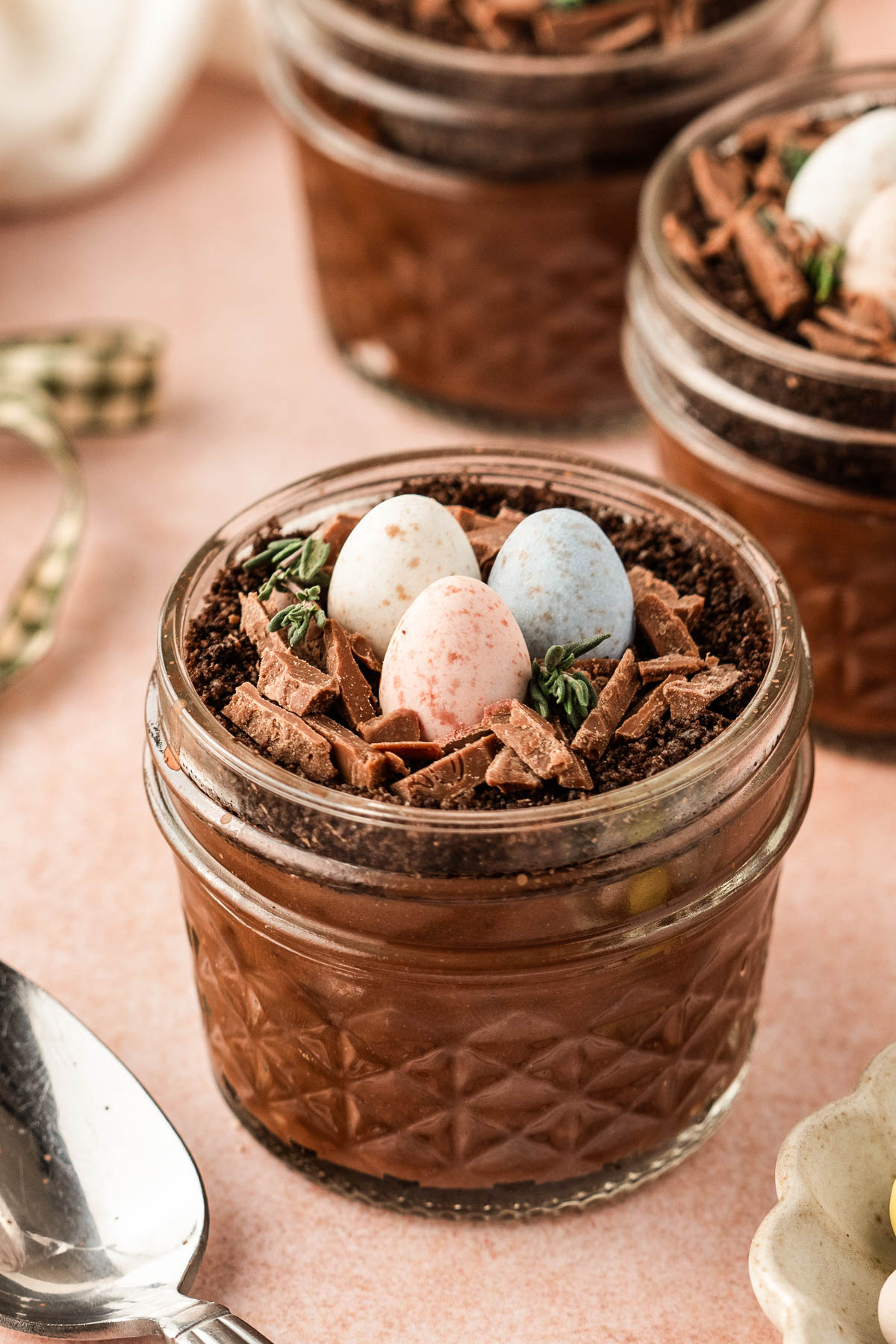 Finished Easter dirt cups layered with chocolate pudding and Oreo crumb “dirt,” topped with chocolate twig nests, speckled pastel mini eggs, and fresh thyme, styled for spring entertaining.