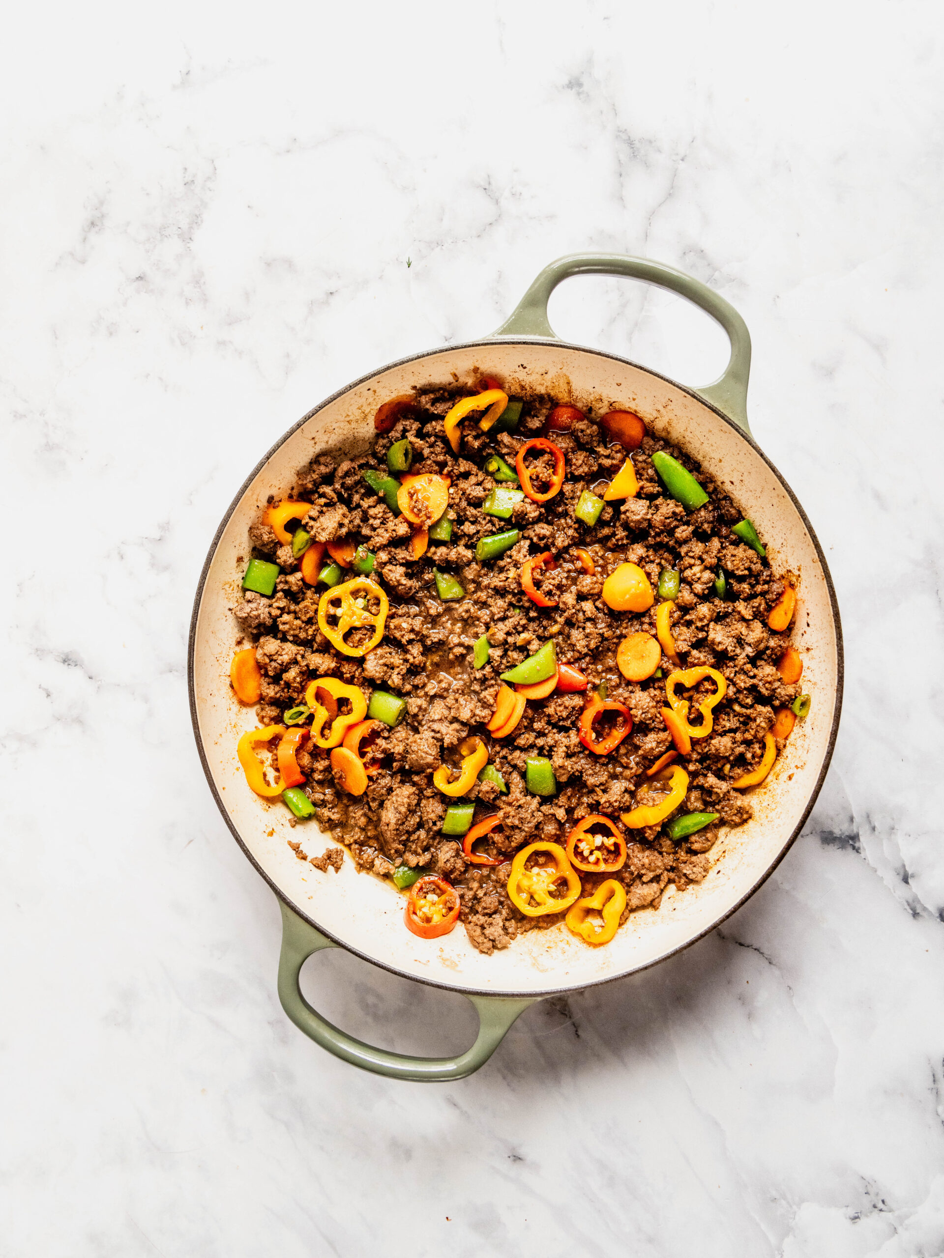 Overhead view of seasoned ground beef cooking with sliced carrots, bell peppers, and sugar snap peas in a skillet for a Korean beef rice bowl, showing colorful vegetables mixed into the savory beef on