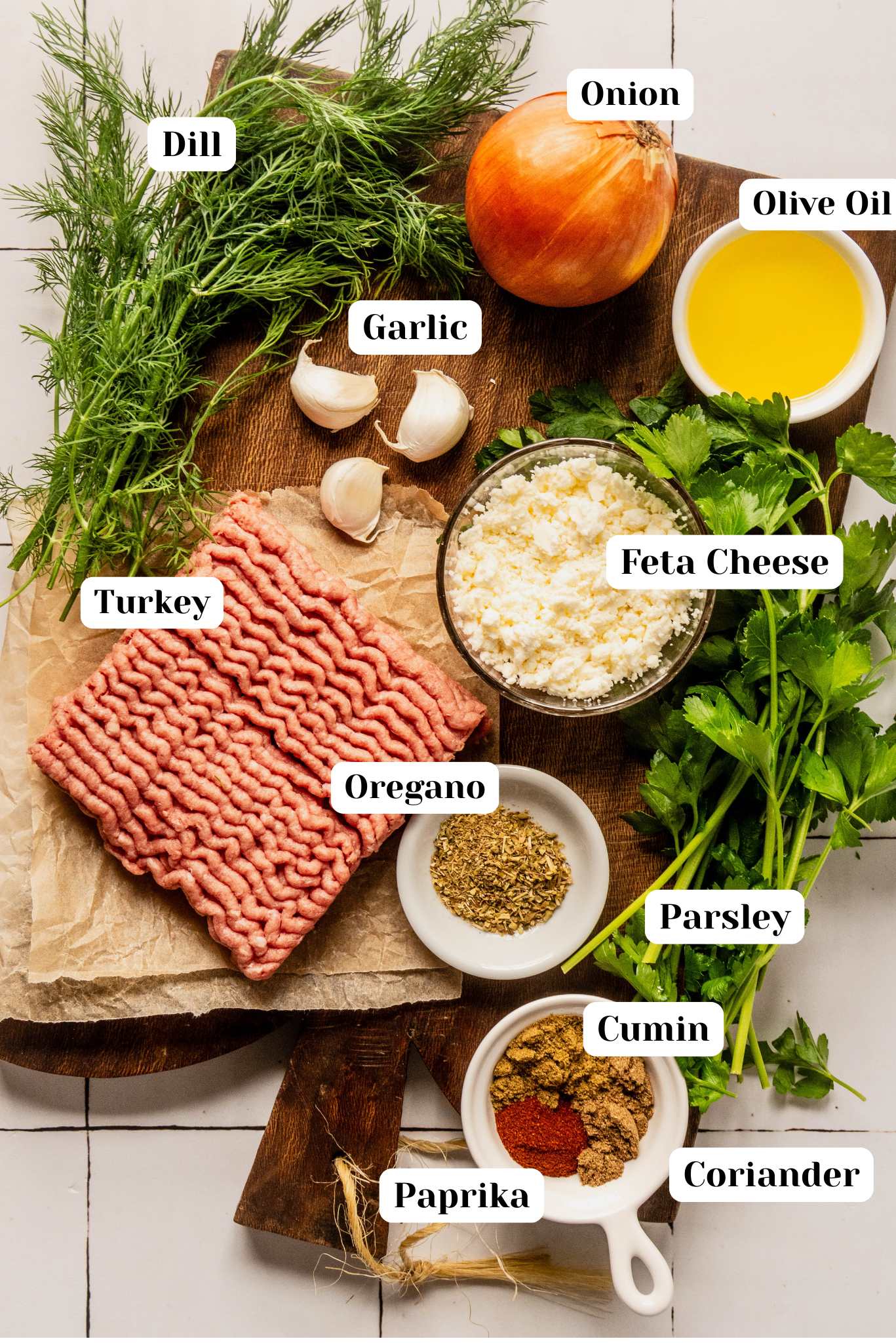 **Alt text:**
Overhead ingredient shot for Greek feta meatballs including ground turkey, feta cheese, onion, garlic, olive oil, dill, parsley, oregano, cumin, coriander, and paprika arranged on a wooden cutting board.
