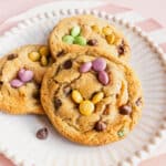 Close-up of soft baked Easter bunny cookies on a white plate, decorated with pastel M&Ms arranged like bunny ears and faces, with chocolate chips throughout.