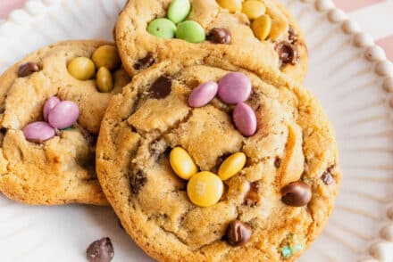 Close-up of soft baked Easter bunny cookies on a white plate, decorated with pastel M&Ms arranged like bunny ears and faces, with chocolate chips throughout.