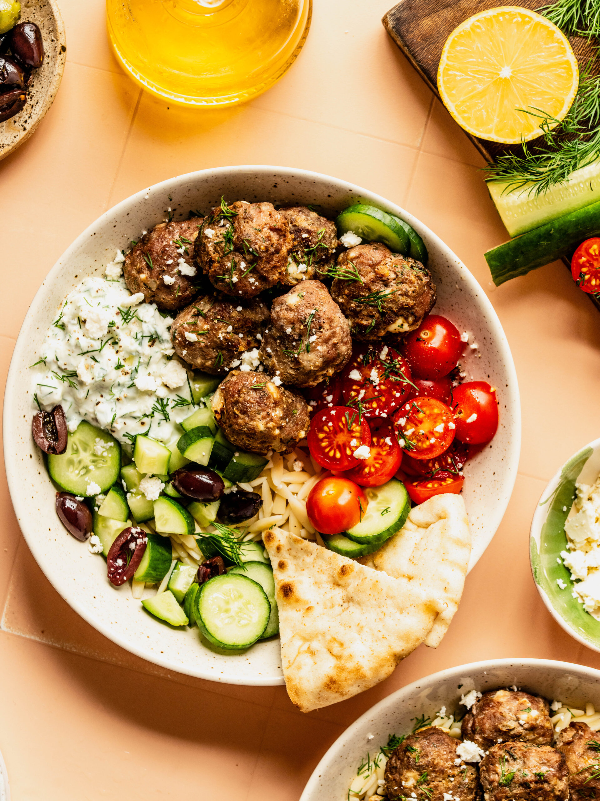 Greek feta meatballs served in a Mediterranean bowl with orzo, cucumbers, cherry tomatoes, olives, tzatziki sauce, and warm pita bread, topped with crumbled feta and fresh dill.