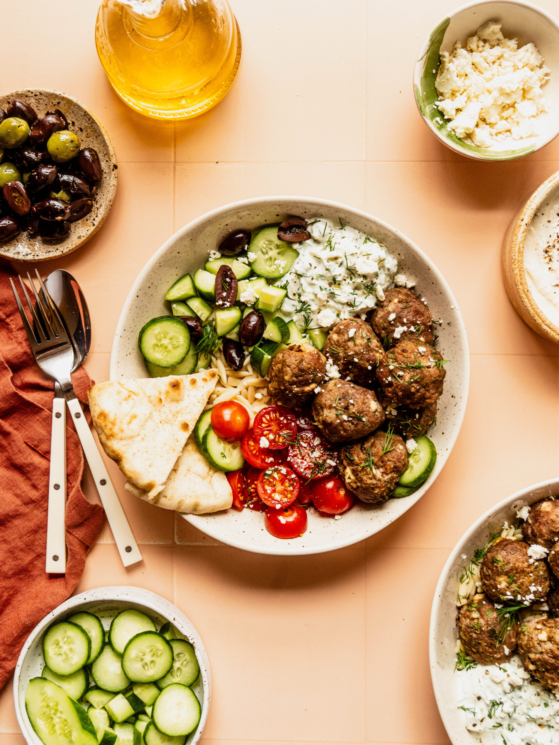 Greek feta meatballs served in a Mediterranean bowl with orzo, cucumbers, cherry tomatoes, olives, tzatziki sauce, and warm pita bread, topped with crumbled feta and fresh dill.