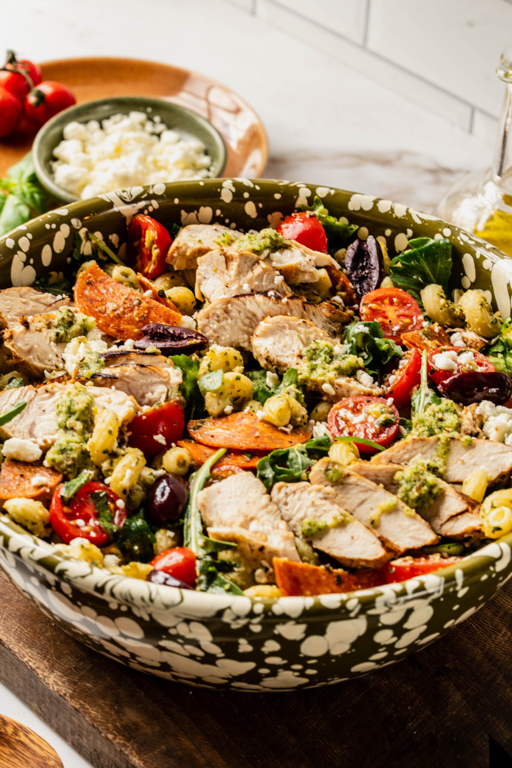 Bright, colorful pasta salad pesto chicken served in a large bowl with corkscrew pasta, grilled chicken slices, cherry tomatoes, kalamata olives, feta cheese, pepperoni, and arugula, all tossed in a vibrant basil pesto.